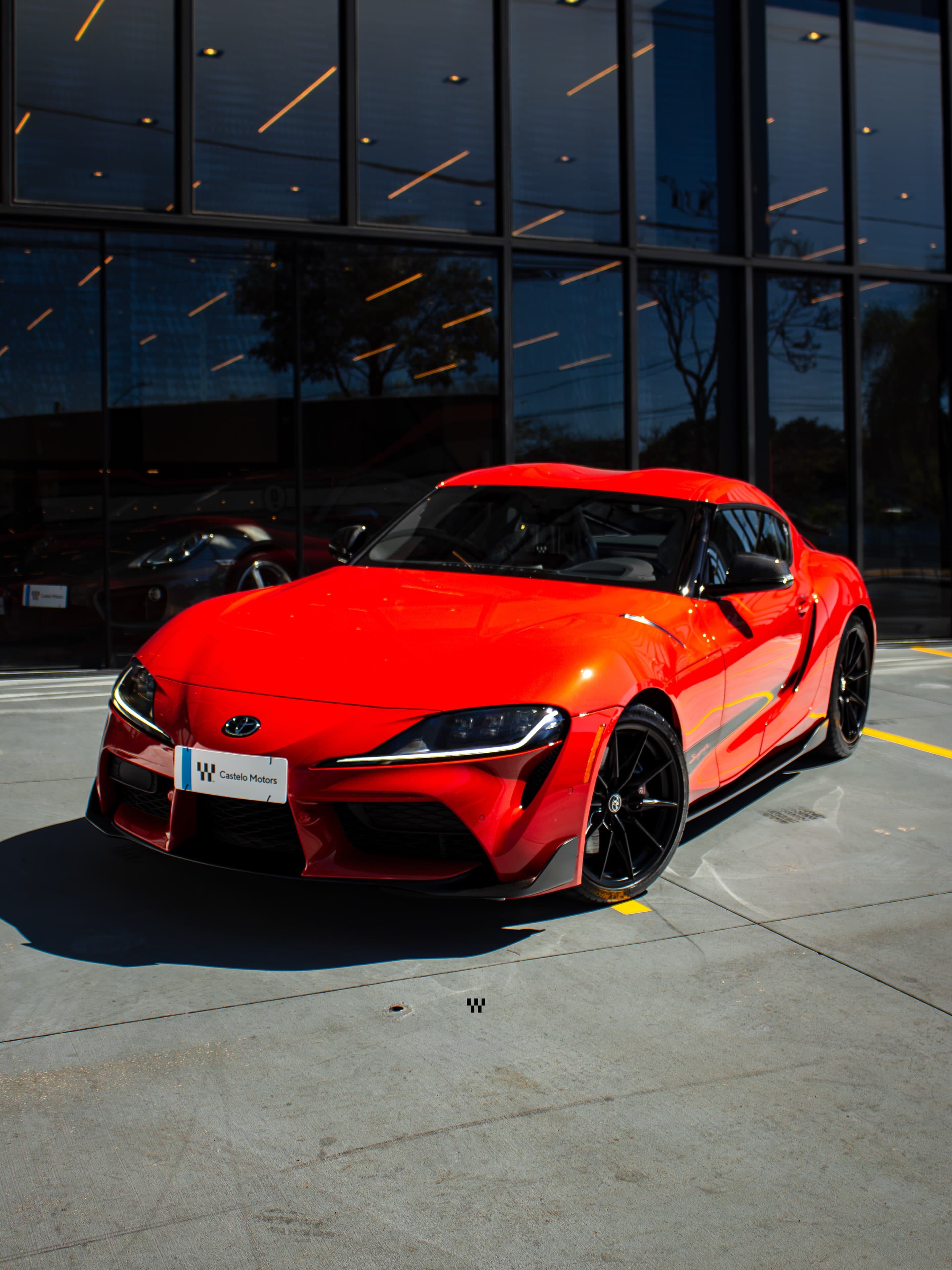 Toyota Supra laranja Mikan Blast com a placa da Castelo Motors, em frente à fachada